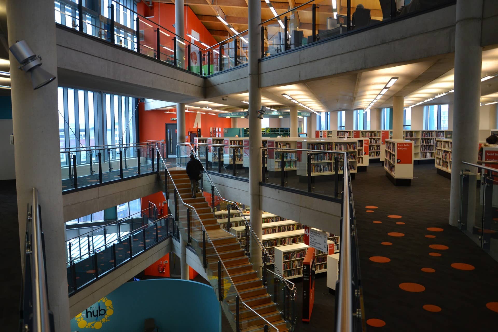 The image is of a person walking down a flight of stairs in a library. The content includes text related to help, travel guides, social aspects, and studying. The tags suggest it is an indoor setting with shelves, aisles, rooms, floors, and ceilings.