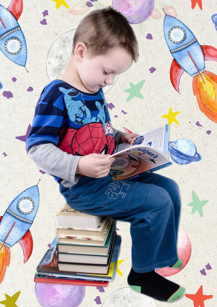 The image shows a boy sitting on books reading a book. The book is titled 'Kayclopedia' and has a drawing of a butterfly on the cover. The boy appears to be engrossed in the book.