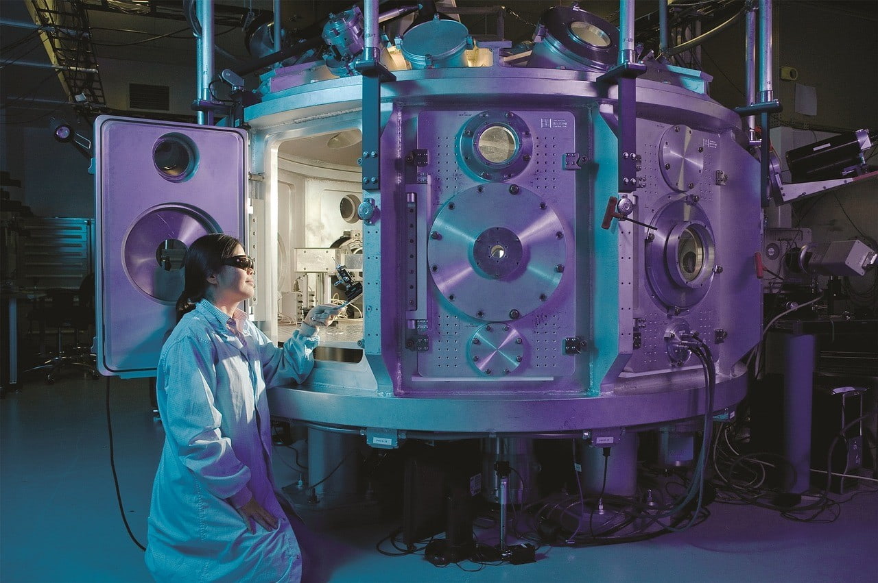 A scientist in a lab coat examines a sizable scientific apparatus in a laboratory setting.